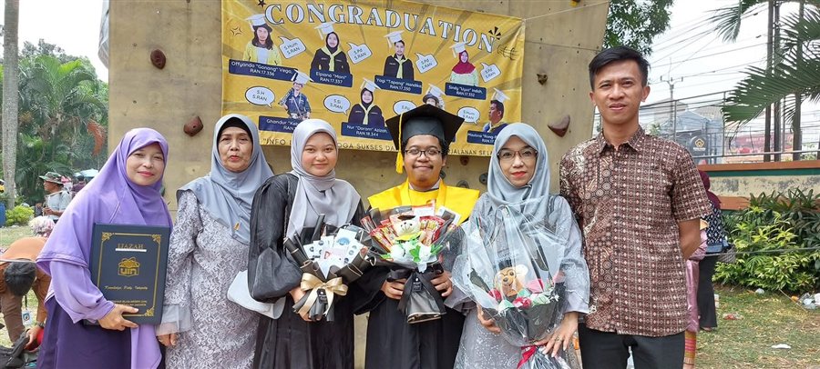 Reva in cap and gown at his graduation, surrounded by his mother, sisters, and father, all holding flowers